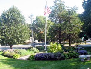 Photo of a round flower and bush garden surrounding a flagpole and flag.